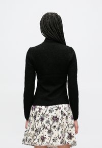 Μαύρο εφαρμοστό πουλόβερ με μακριά μανίκια και υφή με σχέδιο, συνδυασμένο με φούστα σε floral μοτίβο με μοβ και πράσινες αποχρώσεις.