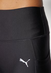 Melnas sporta legginses ar gludu tekstūru, augstu jostasvieta un baltu Puma logotipu sānos. Iekļauta sānu kabata.