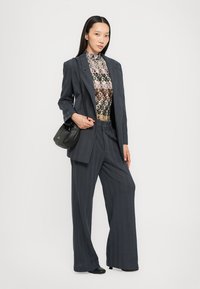 Completo su misura di un elegante blu navy con motivo a spina di pesce, giacca oversize, pantaloni a gamba larga, abbinato a un top colorato con motivo e una piccola borsa nera.