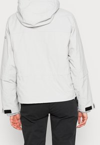 Light gray, cropped jacket with a textured finish, adjustable hood, and Velcro straps on the sleeves. Features a clean, minimalist design.