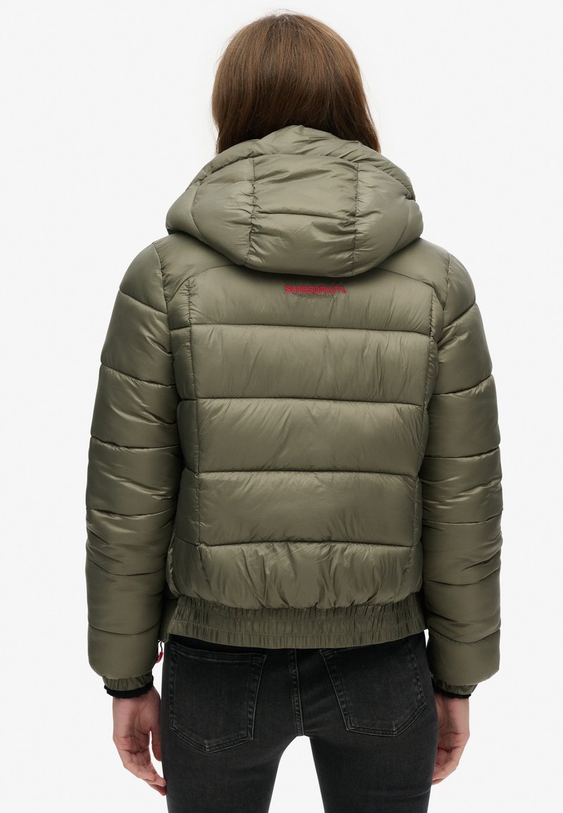 Olijfgroene pufferjack met capuchon, gequilt ontwerp, elastische tailleband en rood logo op de achterkant. Glad, glanzend materiaal.