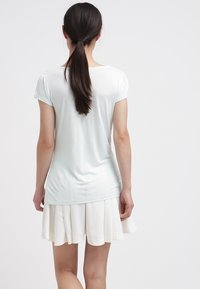 Camisa verde claro de manga corta con un corte relajado, combinada con una falda blanca con pliegues. Textura suave, diseño sencillo, sin patrones visibles.