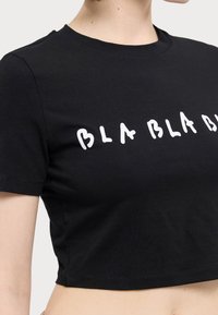 Czarny krótki t-shirt wykonany z bawełny, z białym, rzeźbiarskim napisem "BLA BLA BLA" na przodzie.