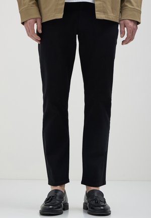 Pantaloni in denim neri con vestibilità slim, caratterizzati da una silhouette pulita e dettagli di cucitura discreti, abbinati a mocassini neri.