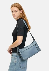 Niebieska skórzana torba na ramię o gładkim wykończeniu, z zamykaną komorą i regulowanym paskiem. Posiada prostokątny kształt i minimalistyczny design.