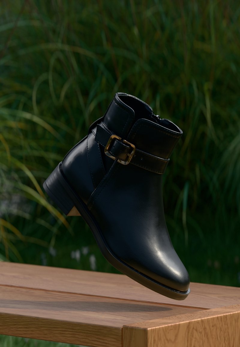Bottine en cuir noir avec une boucle dorée, légèrement surélevée au-dessus d'une surface en bois, fond de feuillage vert.
