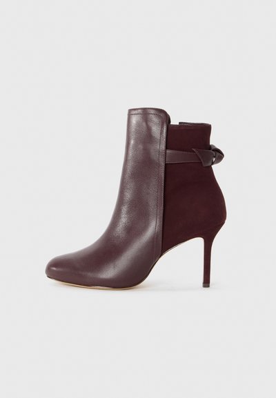 Burgundy ankle boot with a sleek leather finish and a soft suede panel, featuring a high stiletto heel and a bow accent at the back.