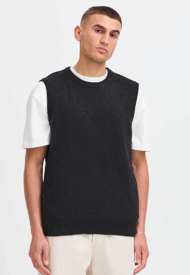Czarny dzianinowy sweter bez rękawów z okrągłym dekoltem, noszony na białej koszulce z krótkim rękawem, o luźnym kroju i prostym wz design.