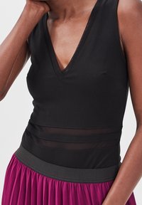 Body noir à col en V avec des panneaux transparents à la taille, accompagné d'une jupe fuchsia plissée avec une ceinture texturée noire.