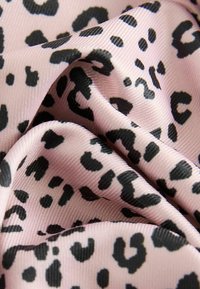 Tissu imprimé léopard en rose avec des taches noires, présentant une texture lisse et un léger éclat, plié pour montrer les détails du motif et le superposition.