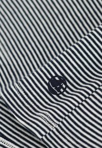 Marineblau- und weißgestreifter Stoff mit einer weichen Textur; hat ein kleines Logo in der oberen Ecke nahe dem Saum.