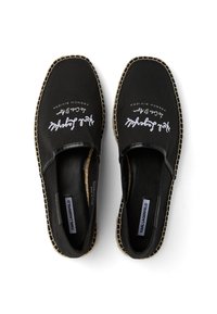 Paire d'espadrilles noires à enfiler avec coutures blanches et texte manuscrit blanc sur le dessus, étiquetées Karl Lagerfeld à l'intérieur.