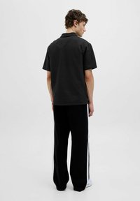 Polo noir à col avec un tissu texturé, associé à un pantalon noir ample avec des rayures blanches sur les côtés. Conçu pour le confort et la tenue décontractée.