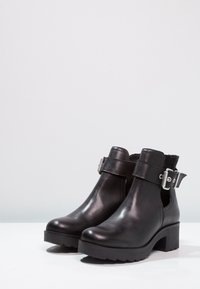 Czarne skórzane botki za kostkę z szerokim paskiem i srebrną klamrą, strukturalnymi panelami bocznymi, grubym obcasem i żłobioną podeszwą.