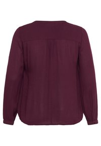 Dlouhá burgundská blůza se volným střihem, lehkým materiálem, sklady na zadní části a knoflíkovými manžetami. Hladká textura, kulatý výstřih.