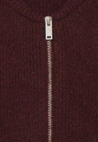 Suéter burdeos con cremallera y textura acanalada. Cuenta con una cremallera de metal plateado en el centro. Tejido suave, estilo casual.