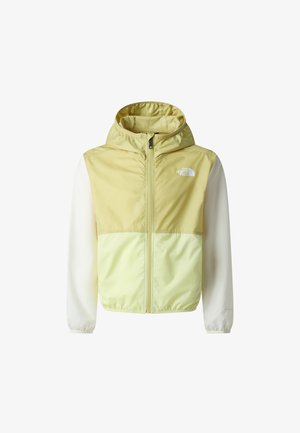 Chaqueta cortavientos en verde claro y crema, pantalones cortos negros y zapatillas beige. La chaqueta tiene una cremallera frontal y un detalle de logo. Texturas suaves.