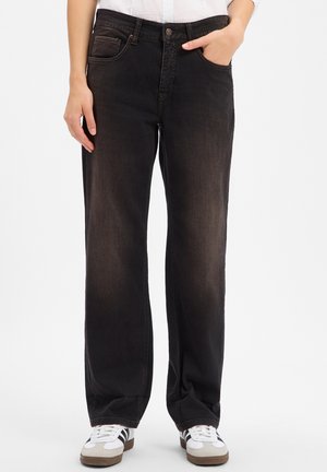 Persoon die zwarte vervaagde rechte jeans draagt met één hand in de zak en witte sneakers met zwarte strepen.