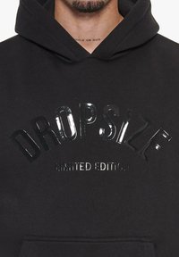 Svart hettegensere med en glossaktig, opphøyd tekstdesign som sier "DROPSIZE" i en bue, med "LIMITERT UTGAVE" under.