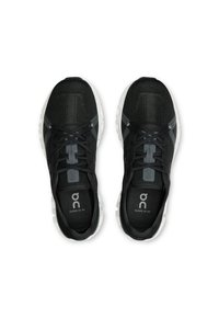 Chaussures de sport noires avec une tige en mesh texturé, bout rond, lacets ajustables et semelle en mousse blanche. Marque sur la languette.