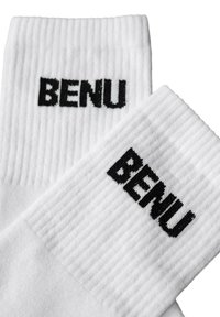 Białe prążkowane skarpetki za kostkę z napisem "BENU" utkanym czarną nicią blisko górnej mankietu, pokazane na białym tle, częściowo nałożone na siebie.