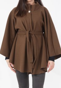 Bruine cape-achtige buitenlaag met een hoge kraag, knoopsluiting aan de voorkant en een ceintuur om te strikken. De stof lijkt zacht met een gladde textuur.