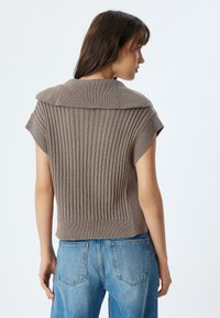 Brauner Strickpullover mit gerippter Textur, weitem Kragen und Kurzarm, kombiniert mit blauen Jeans.