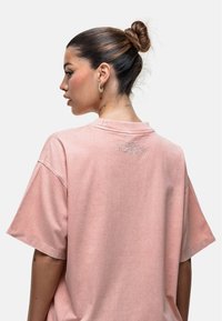 Jasnoróżowy, oversize'owy t-shirt z krótkimi rękawami i okrągłym dekoltem. Posiada subtelny haftowany napis na plecach. Miękka, teksturowana tkanina.