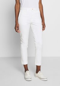 Vita bomullscropbyxor med smal passform och knappstängning. Har sidofickor och uppvikt fåll, tillsammans med vita sneakers.