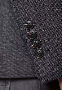 Czarny szary materiał marynarki z teksturowanym splotem. Ma cztery czarne guziki z napisem "LANCERTO" na nich, przyszyte u mankietu.