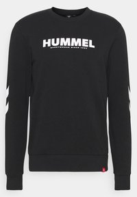 Svart crewneck genser med hvit "HUMMEL" tekst og logo, samt striper på ermene og ribbestrikkede mansjetter og kant.