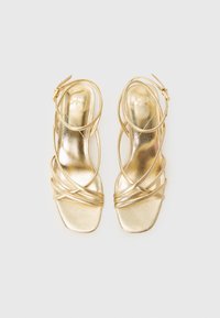 Gold metallic sandals with a square toe, thin crisscross straps, and an ankle buckle. Smooth texture with a glossy finish.