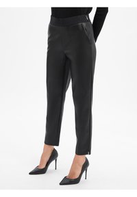 Pantaloni in ecopelle nera con una cintura alta, pieghe frontali e tasche laterali. Abbinati a tacchi a spillo neri per un look elegante.