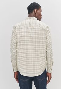 Checkered long-sleeve shirt in light fabric. Features small squares in beige and brown. Tailored fit with a rounded hem and single-button cuffs.