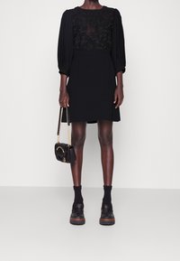 Černé šaty s průsvitnou květinovou výšivkou na živůtku, s vykasanými rukávy a rovnou sukní. Kombinované s černou kabelkou a masivními botami.