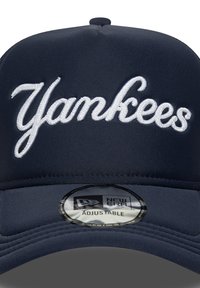 Gorra de béisbol azul marino con bordado blanco de "Yankees". Presenta una parte delantera estructurada, correa ajustable y una pegatina del logo "New Era" en la visera.