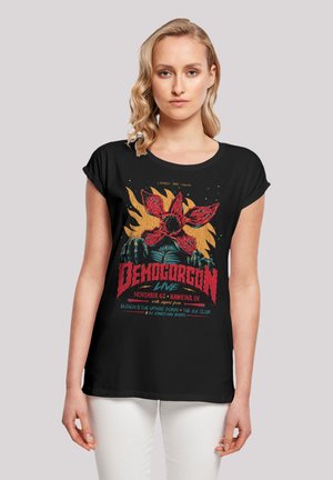 Schwarzes T-Shirt mit buntem Demogorgon-Graphic und Veranstaltungstext, mit kurzen Ärmeln und lockerer Passform, aus weichem Baumwollmaterial.