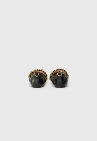Black leather shoes with a rounded shape, featuring a gold chain accent and a gathered texture at the back. Smooth interior finish.