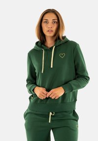 Grøn hætte sweatshirt lavet af blødt stof, som har et guld hjerte-logo og lyse snore. Den har en afslappet pasform og ribbede manchetter.