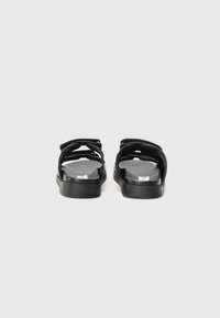 Svarte sandaler med et minimalistisk design, doble justerbare stropper, flat såle og en jevn finish. Åpen bakdel for enkel påkledning.