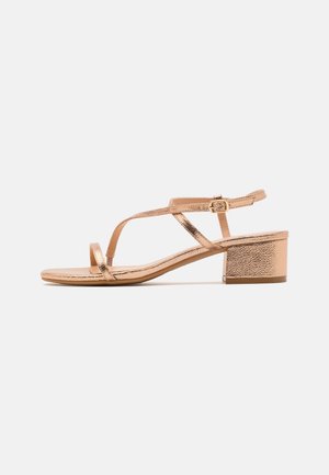 Sandaal met lage blokhak in roségoud metallic, met dunne kruisbandjes en een verstelbare enkelgesp.