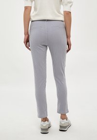 Pantalon léger à rayures grises et blanches, avec une coupe ajustée, poches latérales et ourlets courts. Associé à des baskets blanches.