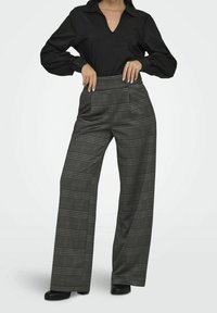 Schwarzes Langarmshirt mit V-Ausschnitt und gepufften Ärmeln, kombiniert mit grauen karierter Hose mit weitem Bein, die über vordere Reißverschlusstaschen und eine glatte Textur verfügt.