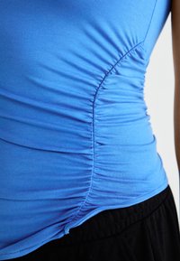 Top de tip tank, de culoare albastră, cu detalii pliate pe laterale; realizat dintr-un material neted și elastic; asortat cu pantaloni negri.