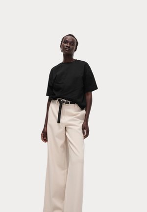 T-shirt en coton noir surdimensionné associé à un pantalon large taille haute crème. Présente une fine ceinture noire pour un détail supplémentaire.