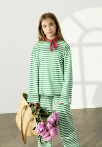 Haut à manches longues rayé vert et blanc et pantalon, avec une écharpe rouge et un panier tissé contenant des pivoine roses. Tissu en coton décontracté, coupe relaxée.