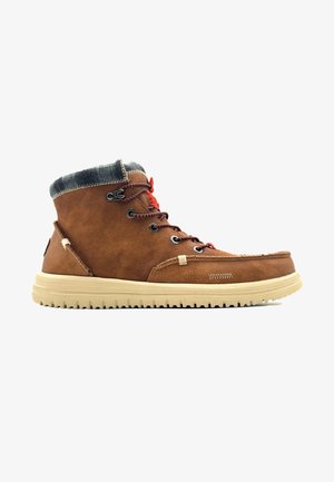 Stivale a caviglia in pelle marrone con risvolto in tessuto, lacci rossi, suola in gomma beige e cuciture decorative. Presenta occhielli in metallo e un logo laterale.