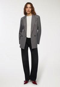 Szary marynarka w prążki z klapami, z podwójnym zapięciem na guziki, zestawiona z białą koszulą i czarnymi spodniami typu wide-leg, uzupełniona czerwonymi czółenkami w szpic.