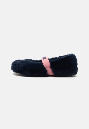 Schwarzer, flauschiger Hausschuh mit einem pinken Gummiband quer über dem Fuß, auf schlichtem, hellem Hintergrund abgebildet.