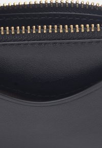 Gros plan sur deux fermetures éclair parallèles en métal doré sur un tissu en cuir noir texturé.